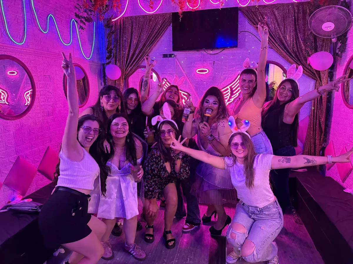 Amigas celebrando con los brazos arriba bajo luces de neón en el Club de Princesas